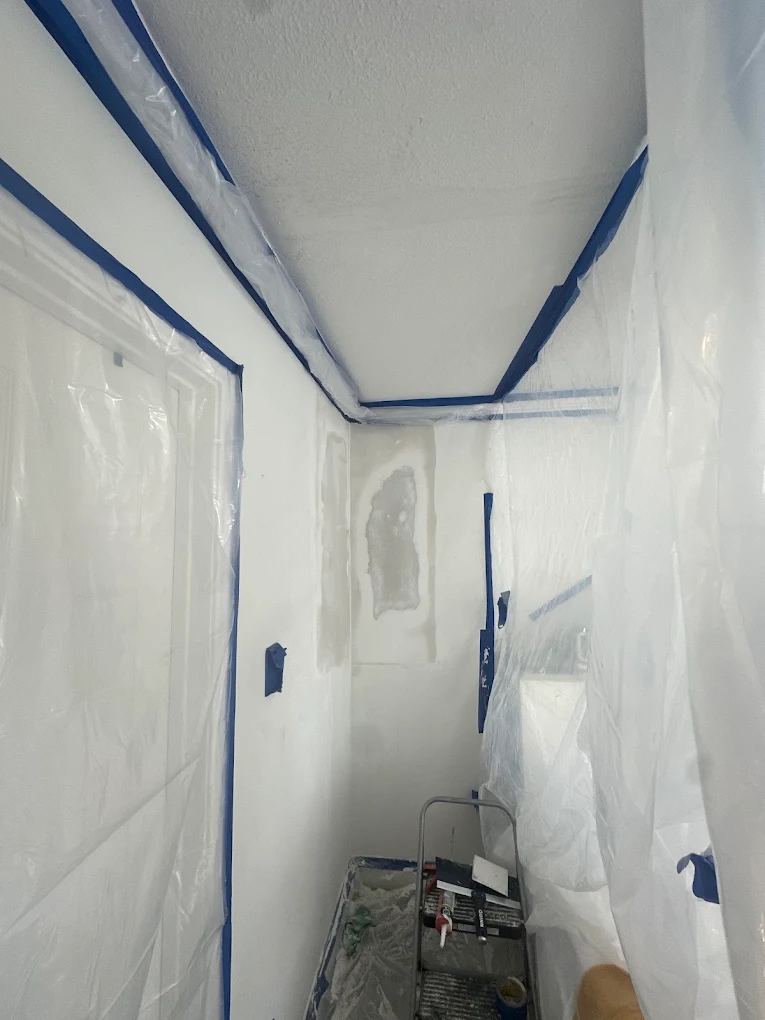 Hallway masked with plastic and tape with a fresh drywall patch floated and ready for paint